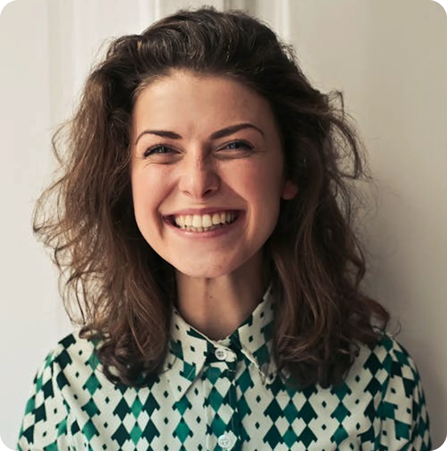 Smiling woman with curly brown hair wearing a patterned green and white collared shirt.